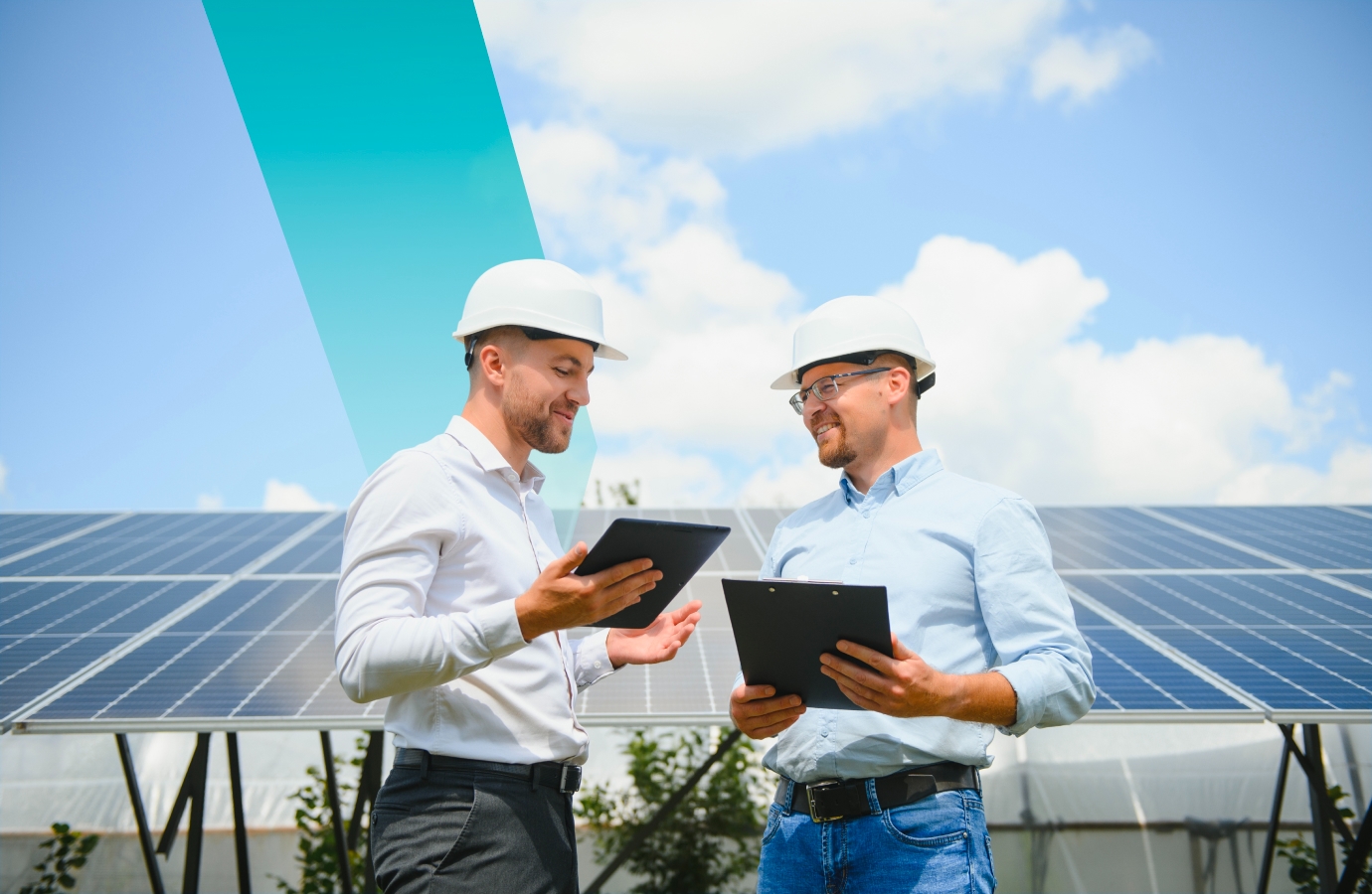 Two professionals in hard hats discussing solar energy with tablets and clipboards, standing in front of a solar panel array under a sunny sky.